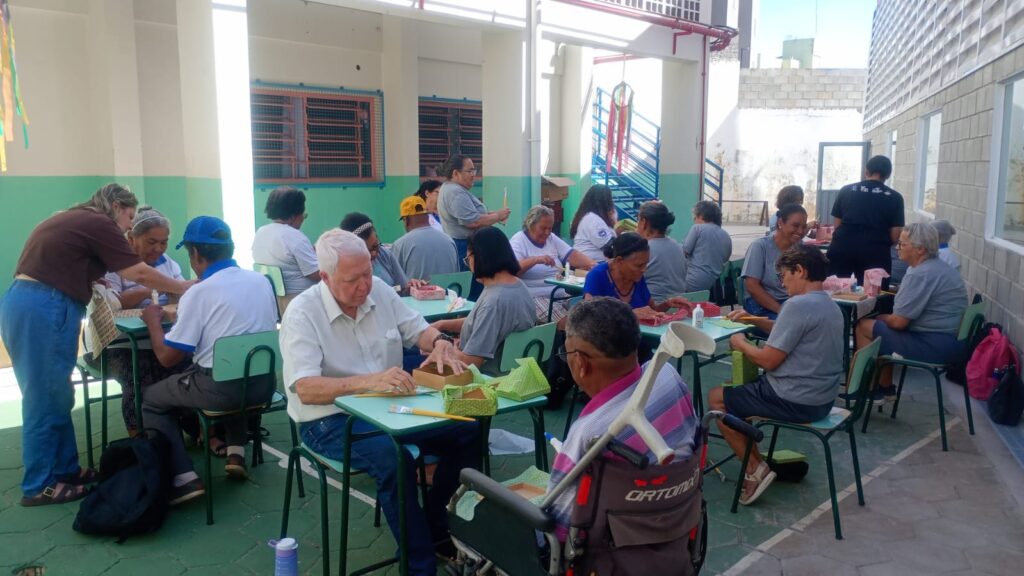 Idosos fazem decupagem em caixas de madeira em mesas ao ar livre